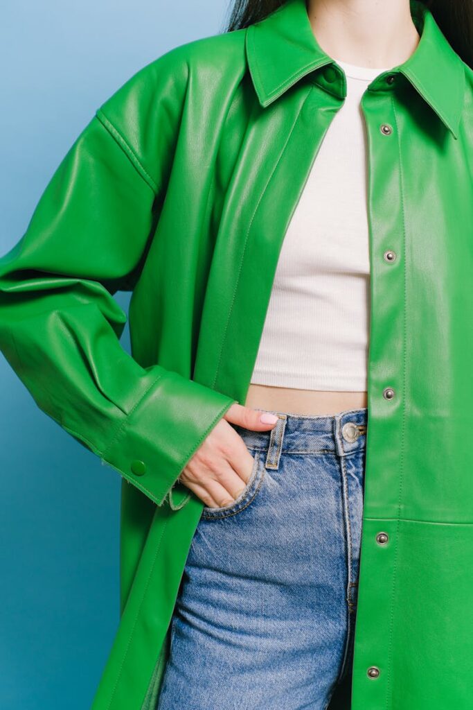 Stylish woman in a green coat and jeans against a light blue background.