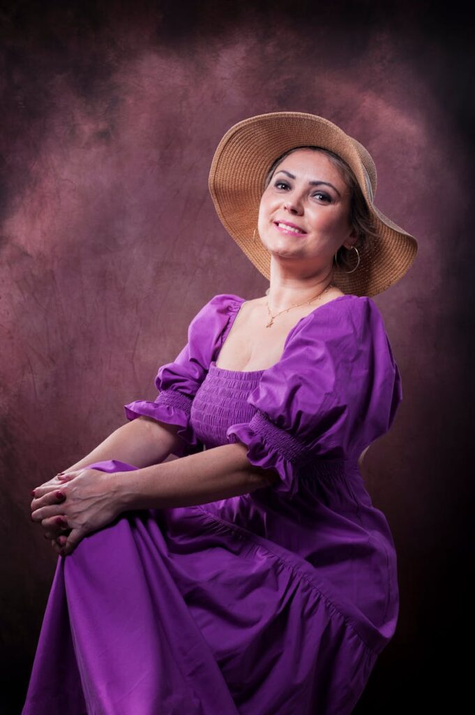 Portrait of a smiling woman in a purple dress and brown hat, studio setting.