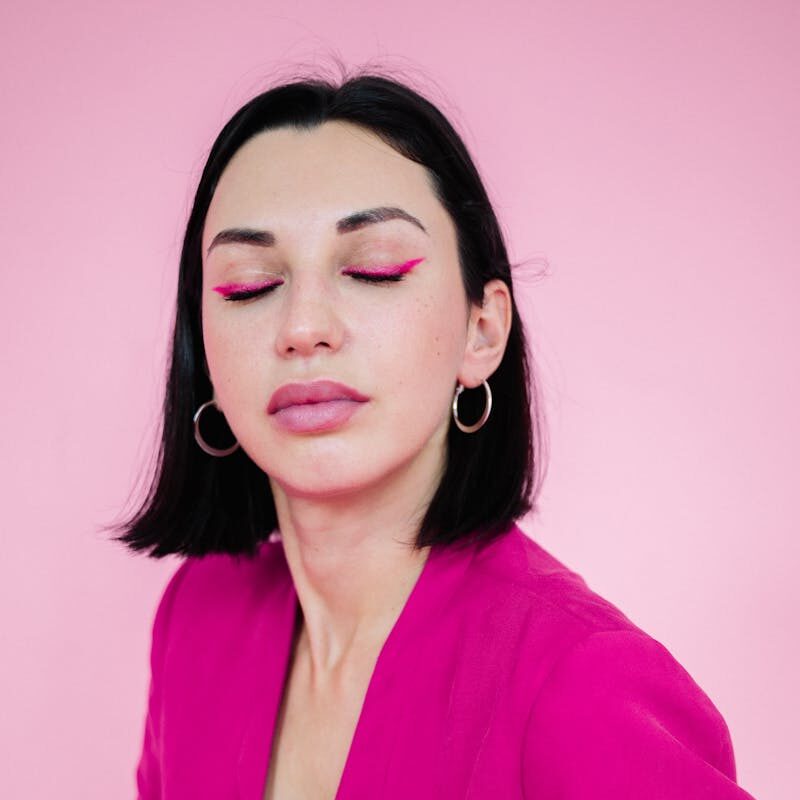 Portrait of a woman in a pink blazer posing with elegance against a pink background.
